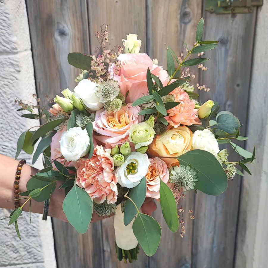 Brautstrauß mit Rosen, Nelken, Eukalyptusblättern und weiteren Blüten in Pastelltönen vor Holztür