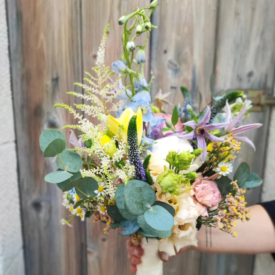 Bunter Blumenstrauß mit verschiedenen Blüten und Eukalyptusblättern vor Holzwand gehalten