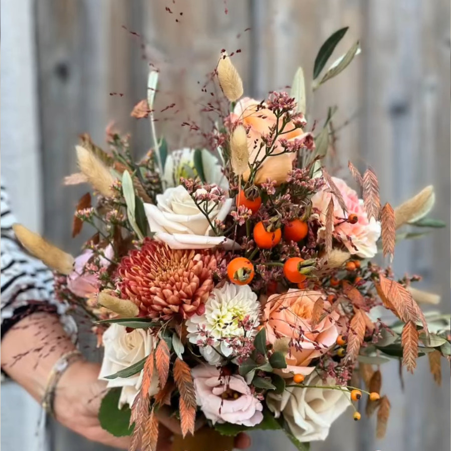 Bunte Blumenstrauß mit Rosen, Chrysanthemen, Beeren und getrockneten Gräsern vor unscharfem Holzhintergrund