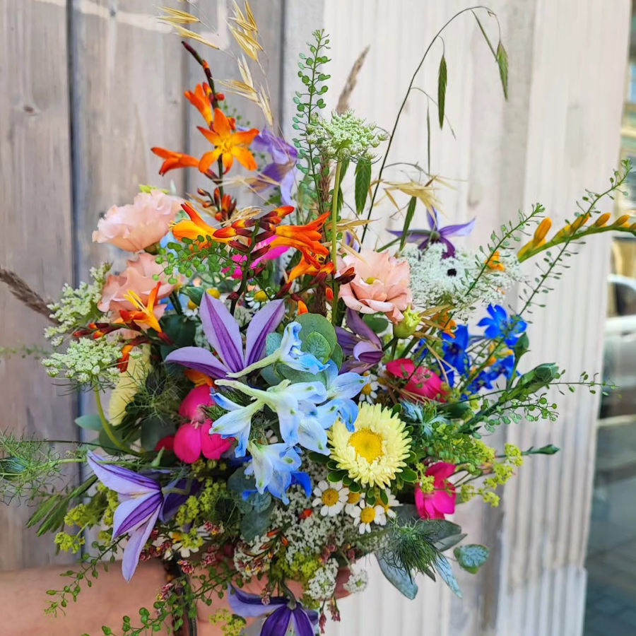 Bunter Blumenstrauß mit verschiedenen Blüten und Gräsern vor einer Holzlattenwand