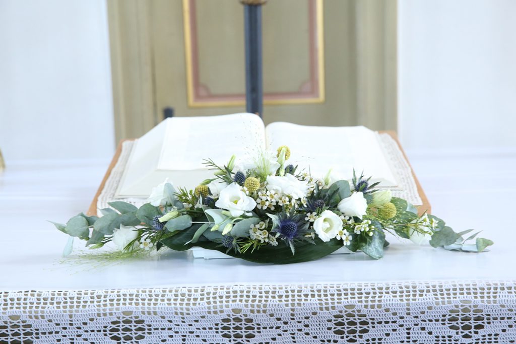 Offenes Buch auf einem Altar mit einem Blumenarrangement aus weißen Blüten und grünen Blättern